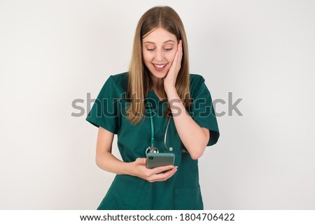 Close-up portrait of Female doctor wearing a green scrubs and stethoscope is on white background holding in hands cell reading sms using new app 5g 