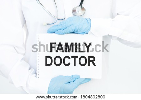 A doctor in medical clothes holds a card with the text FAMILY DOCTOR. Medical concept.