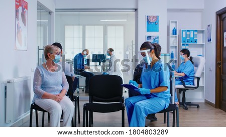Nurse and senior patient going in hospital examination room from waiting area. Doctor inviting old woman for consultation in office. Wearing mask against coronavirus. Royalty-Free Stock Photo #1804803289