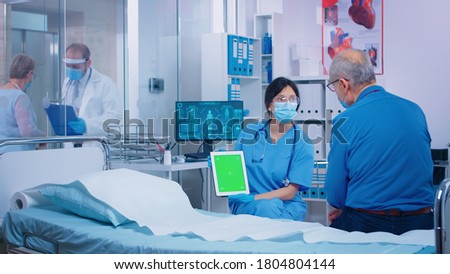Nurse presenting green screen tablet to patient in modern private hospital. Isolated mockup chroma replacement screen on gadget for your app, text, video or digital assets. Easy keying medicine