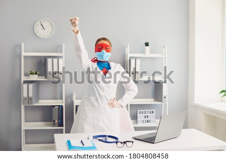 The doctor in a protective mask a superhero suit raised her hand up while standing in the office of the clinic