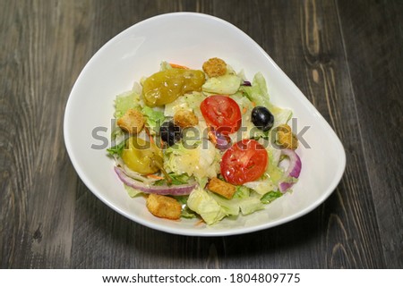 A ceasar salad with tomatoes, purple onion, black olives, pepperoncini peppers and croutons.