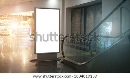 vertical advertise lcd lightbox with white mockup space in airport or mall building near moving staircase inside