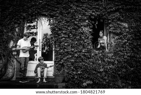 Black and white of two youths playing lutes and serenading a girl sitting in an ivy clad window.
