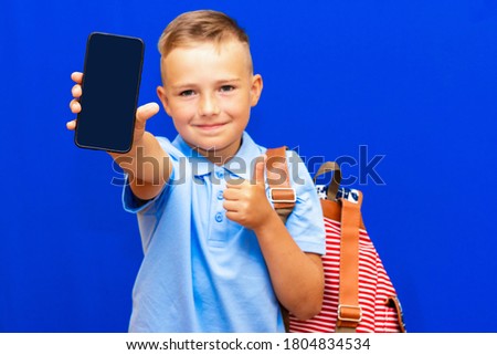 Young schoolboy 9 years old wears blue t shirt holds phone striped red backpack isolated on blue background children studio portrait education lifestyle concept