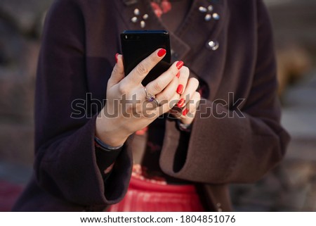 Young woman holding phone in hands with beautiful red manicure. Close up picture outdoor