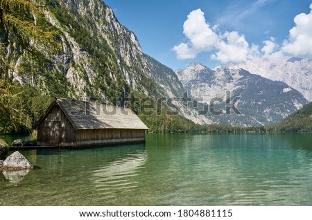 Scenic view of alpine lake Obersee and wooden boathouse surrounded by mountains on a summer day with blue sky and clouds, Schoenau am Koenigssee, Bavaria, Germany, Europe. Famous travel destination. Royalty-Free Stock Photo #1804881115
