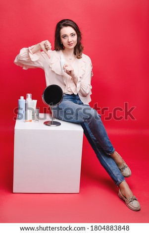 Beautiful woman chooses a cosmetic product, studio photo on a red background. Cosmetology and personal care concept
