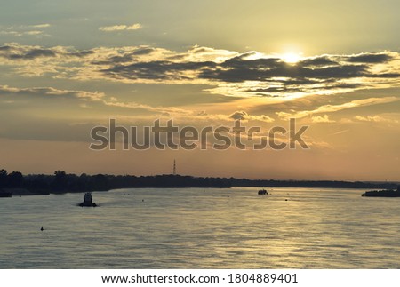 Sunset over the Ob river. The wide water area of the great Siberian river, ripples on the water with light highlights, trees on the horizon, the evening sky with Golden clouds, the bright sun