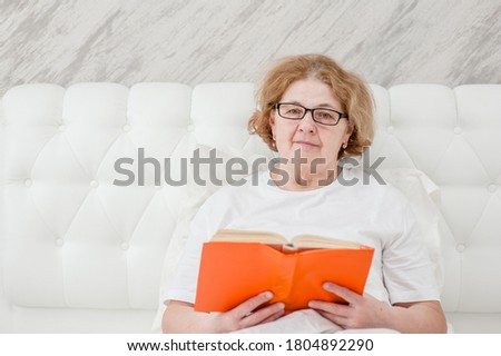Smiling  senior woman with  book on the bed. Empty space for text