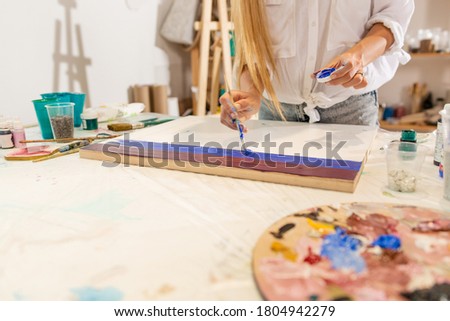 Woman artist painting lgbt flag while standing at table with paints in art studio adding blue color