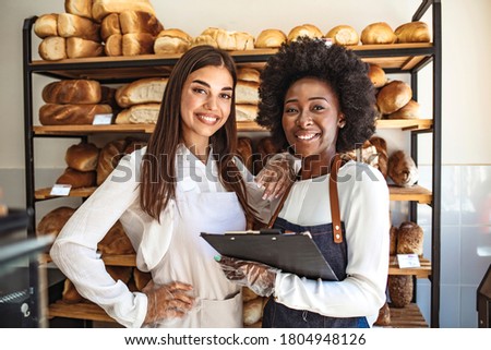 Two beautiful young bakers at the bakery. Shot of two women holding a selection of freshly baked breads in their bakery. Nobody bakes it better than we do