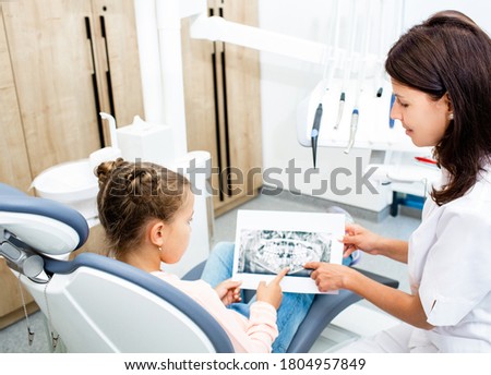 Dentist and little girl in the dental office are looking at an x-ray of the teeth. Kid teeth treatment