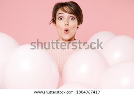 Amazed surprised shocked young brunette woman 20s in knitted casual sweater celebrating birthday holiday party holding bunch of air helium balloons isolated on pastel pink background, studio portrait.