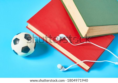 White headphone and old books, toy soccer, football ball on blue background. Audiobook concept. Online education. E-learning. Modern technology