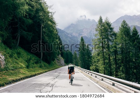 Professional road cyclist on fast and light carbon bicycle descends mountain road in Alps Dolomites. Fit and athletic man on recreational ride trip or training camp, enjoy time outdoors on bike Royalty-Free Stock Photo #1804972684