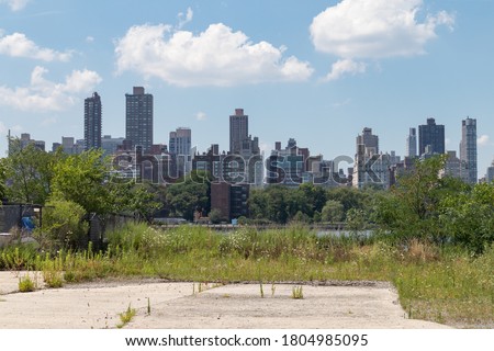 Vacant Land on the Riverfront of Astoria Queens New York with Overgrown Plants and a view of the Roosevelt Island and Manhattan Skylines Royalty-Free Stock Photo #1804985095