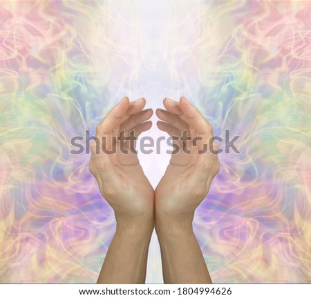 Healers Hands sending high frequency energy out - female cupped hands with shaft of white light against beautiful energy formation background and space for copy 
