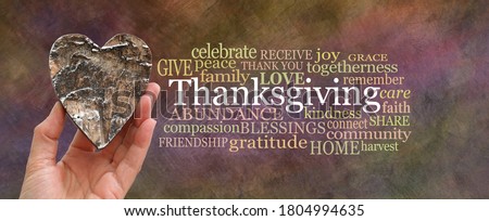 Put some love into Thanksgiving Word Cloud concept - hand holding a rustic brown wooden heart beside a THANKSGIVING word cloud on oil painted warm coloured background
