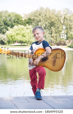 the boy plays the guitar in nature. Park and pond in the summer.