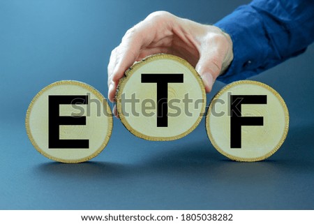 The Concept Of Exchange Traded Funds. A man displays round pieces of wood with the letters ETF on a dark background.