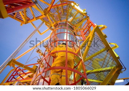 Low angle view of oil worker in coverall and helmet on an industrial steel ladder with safety cage. Heavy industry gas and petroleum plant. Pov with selective focus as safety first concept at work. Royalty-Free Stock Photo #1805066029