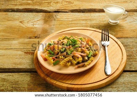 a plate with pasta with ham and mushrooms in a creamy sauce on a table with a fork on a round wooden stand.