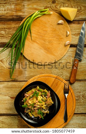 Black plate with pasta with ham and mushrooms in a creamy sauce on the table with a fork near the ingredients.