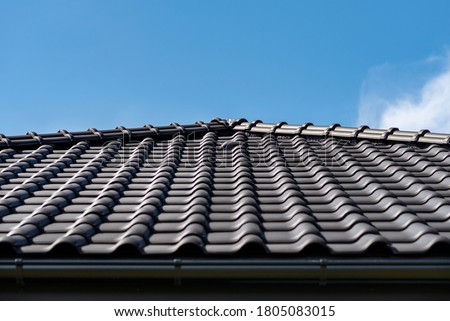 The roof of a single-family house covered with a new ceramic tile in anthracite against the blue sky, visible ceramic ventilation tile on the roof. Royalty-Free Stock Photo #1805083015