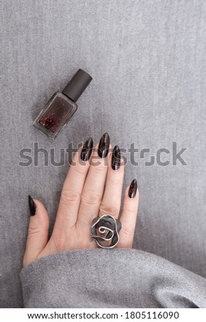 Female hand with long nails and gray black manicure with bottles of nail polish