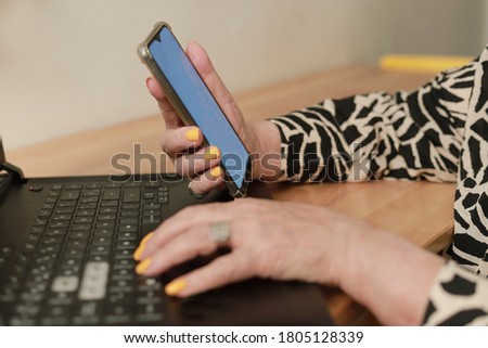 horizontal photo of woman's hands typing on the keyboard of a laptop and holding a mobile