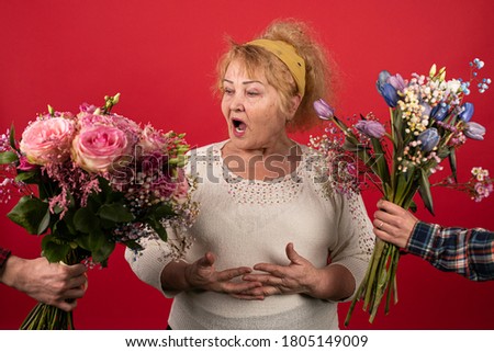 An elderly woman is presented with two bouquets of beautiful flowers at the same time, a woman delighted with an abundance of bright and fragrant surprises, roses, tulips, pink and blue.