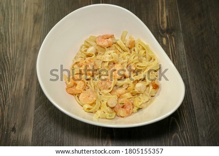 A white bowl with Alfredo fettuccine pasta with shrimp and scallops.