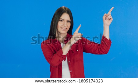 Young woman pointing with her fingers in the upper right corner of the screen on a blue background.