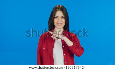 Young woman pointing to the right of the screen with her fingers on a blue background.