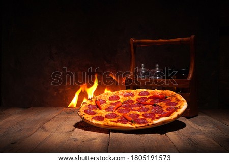 Beautiful Pizza Pepperoni on a rustic wooden table against the fireplace 