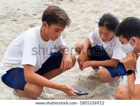 3 Asian kids can been seen playing whilst using a mobile device on a pretty sandy beach in Chiba Japan. A typical scene in-along the Japanese coastline in the summer time.
