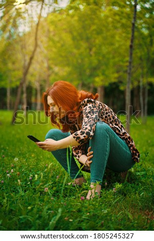 Red-haired young adult woman enjoys mobile photography in the Park taking pictures of flowers