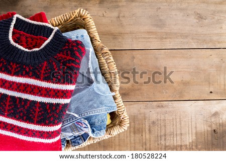 Wicker laundry basket filled with clean fresh washed winter clothes viewed from overhead standing at an angle on rustic wooden boards with copy space on the right