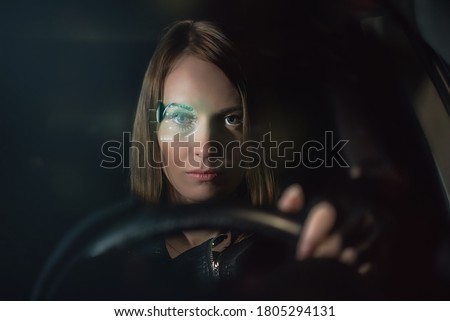 Woman in the sci fi futuristic eyeglasses sits by the car steering wheel.