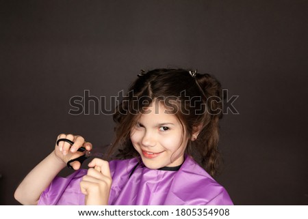 Portrait of a Caucasian young curly-haired girl holds metal scissors at her face on a dark background. The concept of a self-employed hairdresser, home Barber. DIY hair cut during covid-19