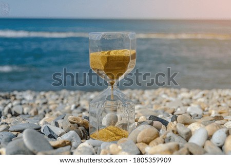 Hourglass on sea stones by the ocean in the sun