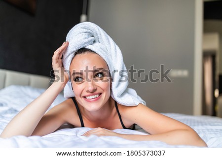 Young woman in towel and bathrobe laying on the bed and looking at the camera.