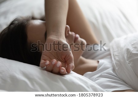 Close up sleepless young woman lying in bed, suffering from insomnia, tired exhausted female covering face with hand, trying to sleep, resting under white warm duvet on soft pillow Royalty-Free Stock Photo #1805378923