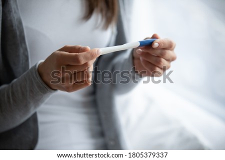 Close up cropped image woman holding plastic pregnancy test kit in hands, sitting on bed at home, young female checking results, fertility maternity concept, gynecological healthcare Royalty-Free Stock Photo #1805379337