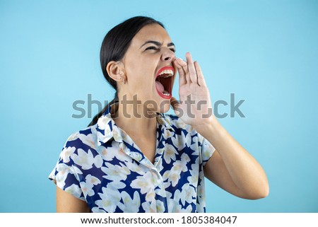 Young beautiful woman over isolated blue background shouting and screaming loud to side with hand on mouth