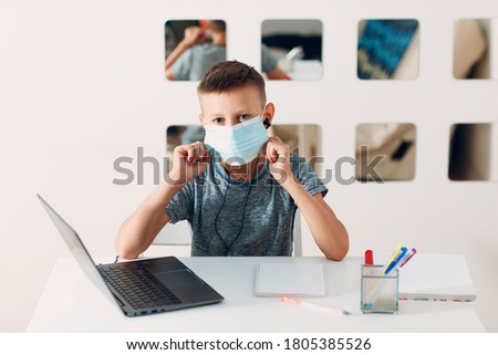 Young boy in headset sitting at table with laptop and medical face mask and preparing to school. Online education concept.