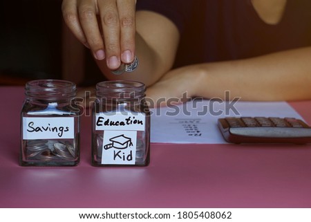 Mom is putting coins in a glass bottle for her child's education after completing her daily income and expenses accounting.