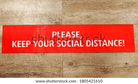red attention safety sign with lettering please keep your social distance on wooden floor of store or supermarket coronavirus concept close upper view