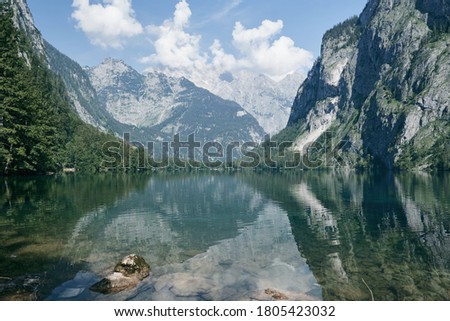 Forested mountain range reflecting in Lake Obersee on a beautiful summer day with blue sky in the Berchtesgaden Alps, Schoenau am Koenigssee, Bavaria, Germany. Royalty-Free Stock Photo #1805423032